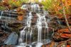 A view of Issaqueena Falls flowing down a rocky, moss-covered cliff surrounded by colorful fall leaves.