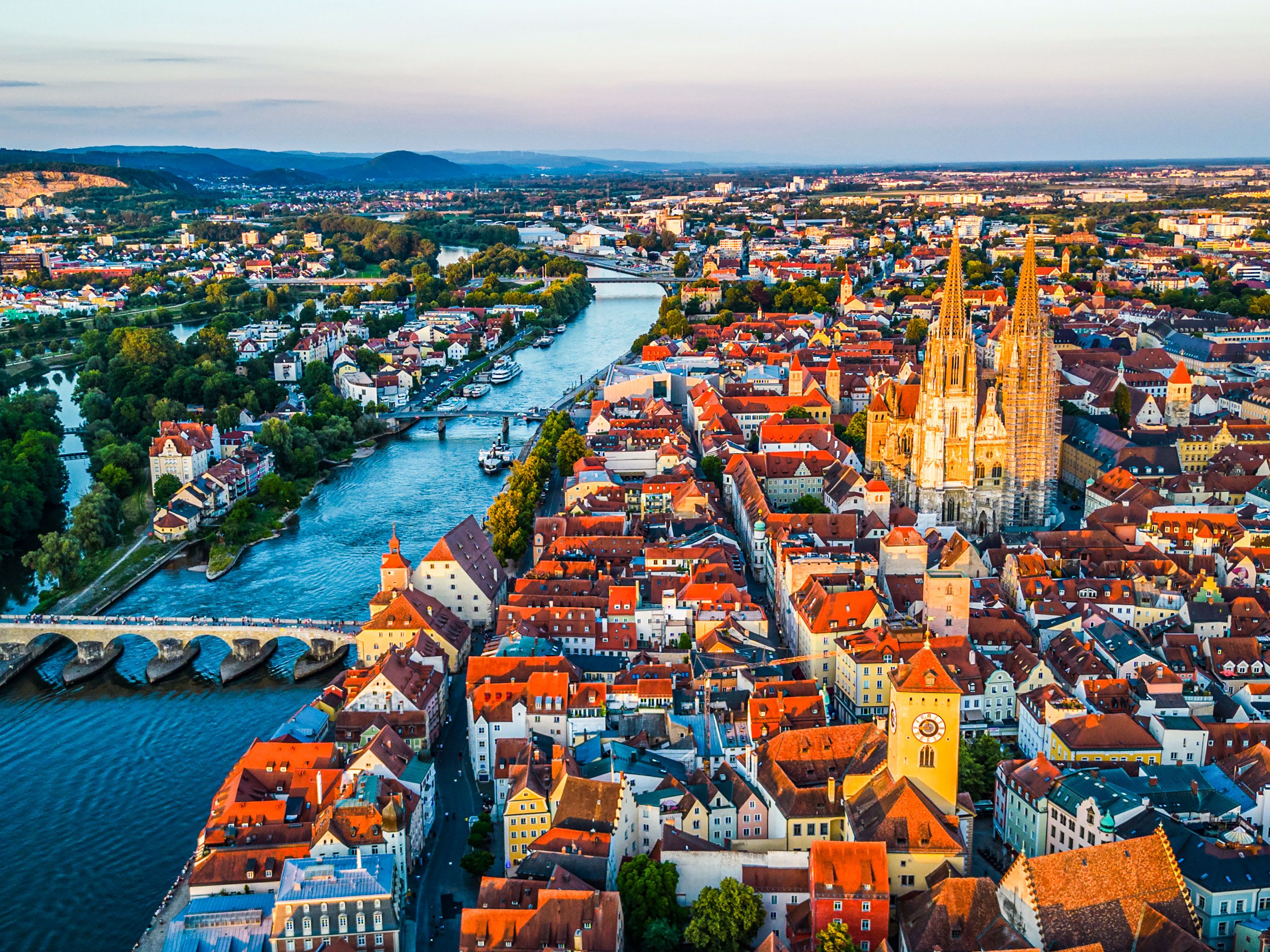 Aerial view of Regensburg at warm glowing sunset with the Stone Bridge over the Danube River and the twin towers of St. Peter’s Cathedral
