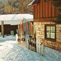 Colourful skis are held upright against a fence outside a chalet at a ski resort covered by thick snow