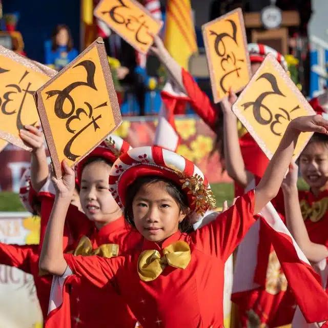 Young girls in red costume wave signs reading "Tết" in the air during the Tết Parade in Wetminster, CA