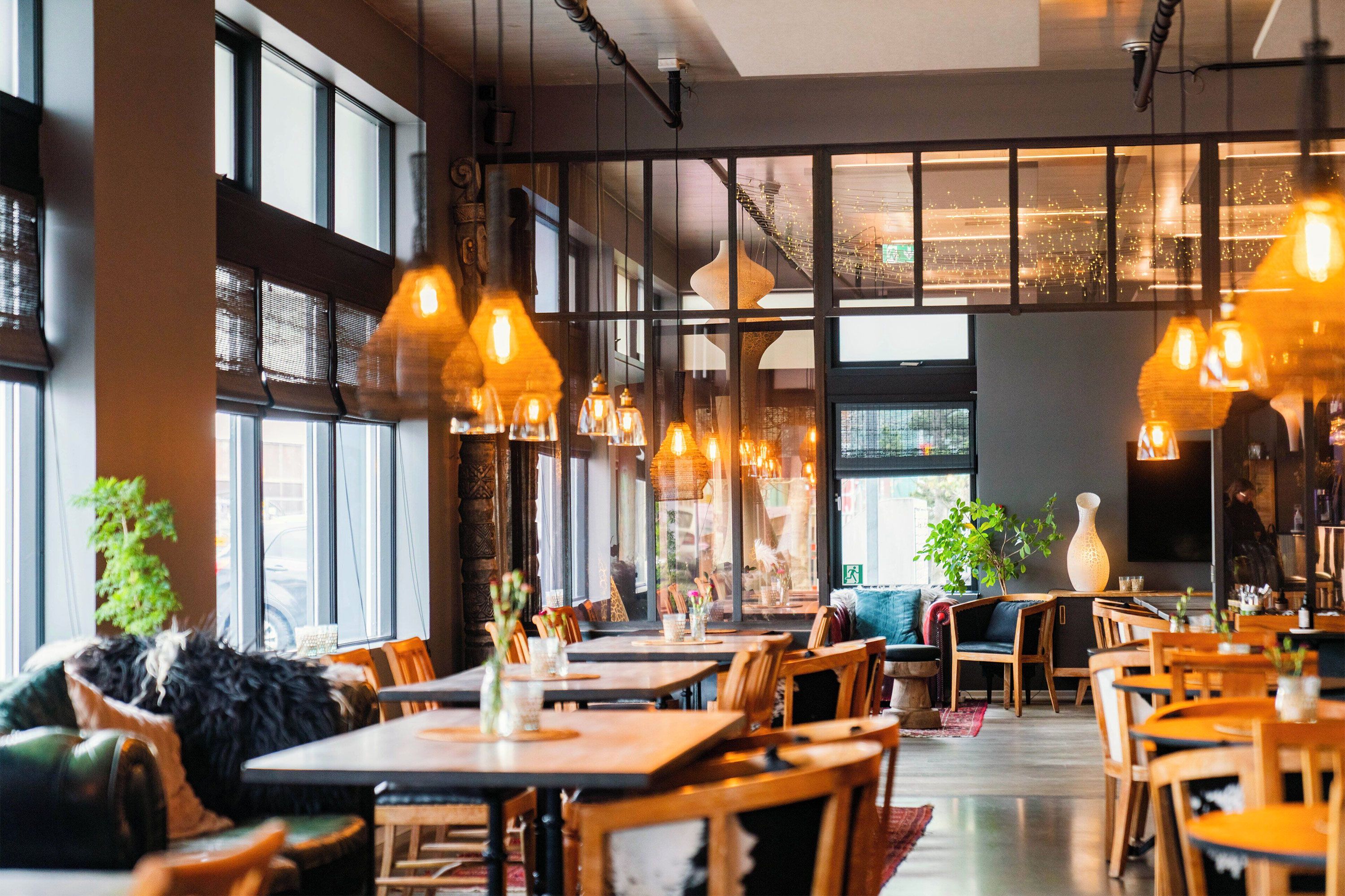 An interior view of a stylish restaurant with wooden tables and chairs, soft warm lights, large windows, and contemporary décor.