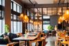 An interior view of a stylish restaurant with wooden tables and chairs, soft warm lights, large windows, and contemporary décor.