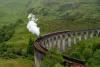 A steam train crossing the Glenfinnan Viaduct surrounded by lush green hills