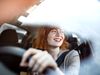 Woman with red hair smiling out car window behind the wheel.