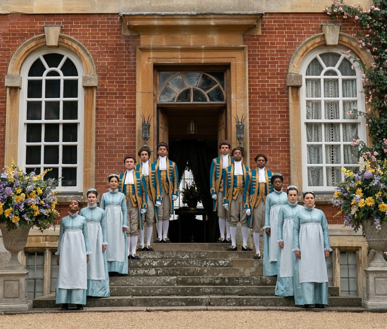 Footmen and maids line the stairway in front of Kingston Bagpuize House, Oxfordshire, in a scene from Bridgerton