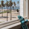 A view of the beach, palm trees, and the Pacific beyond, from the window of the Venice V Hotel; a skateboard leans against the windowsill