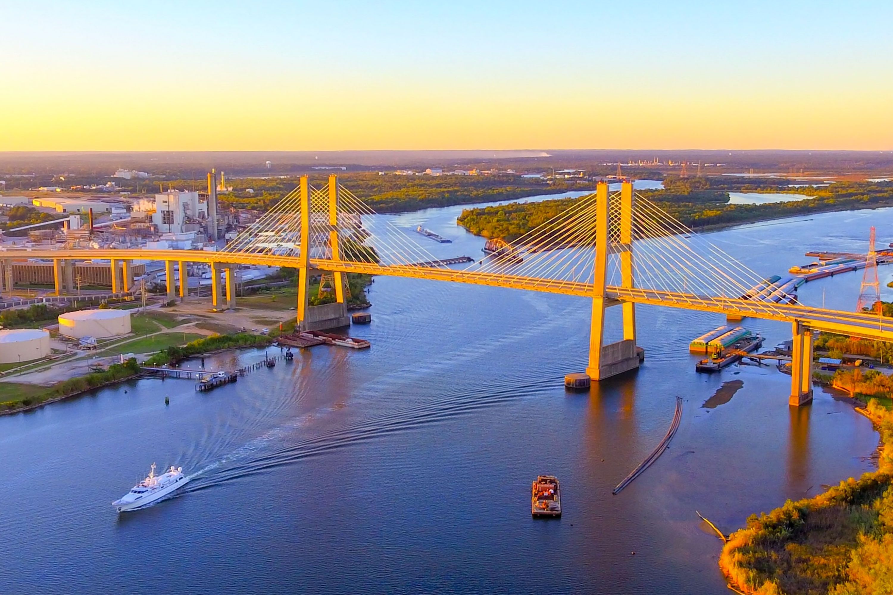 A cable stayed bridge spanning a wide river at golden hour with boats below.
