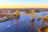 A cable stayed bridge spanning a wide river at golden hour with boats below.
