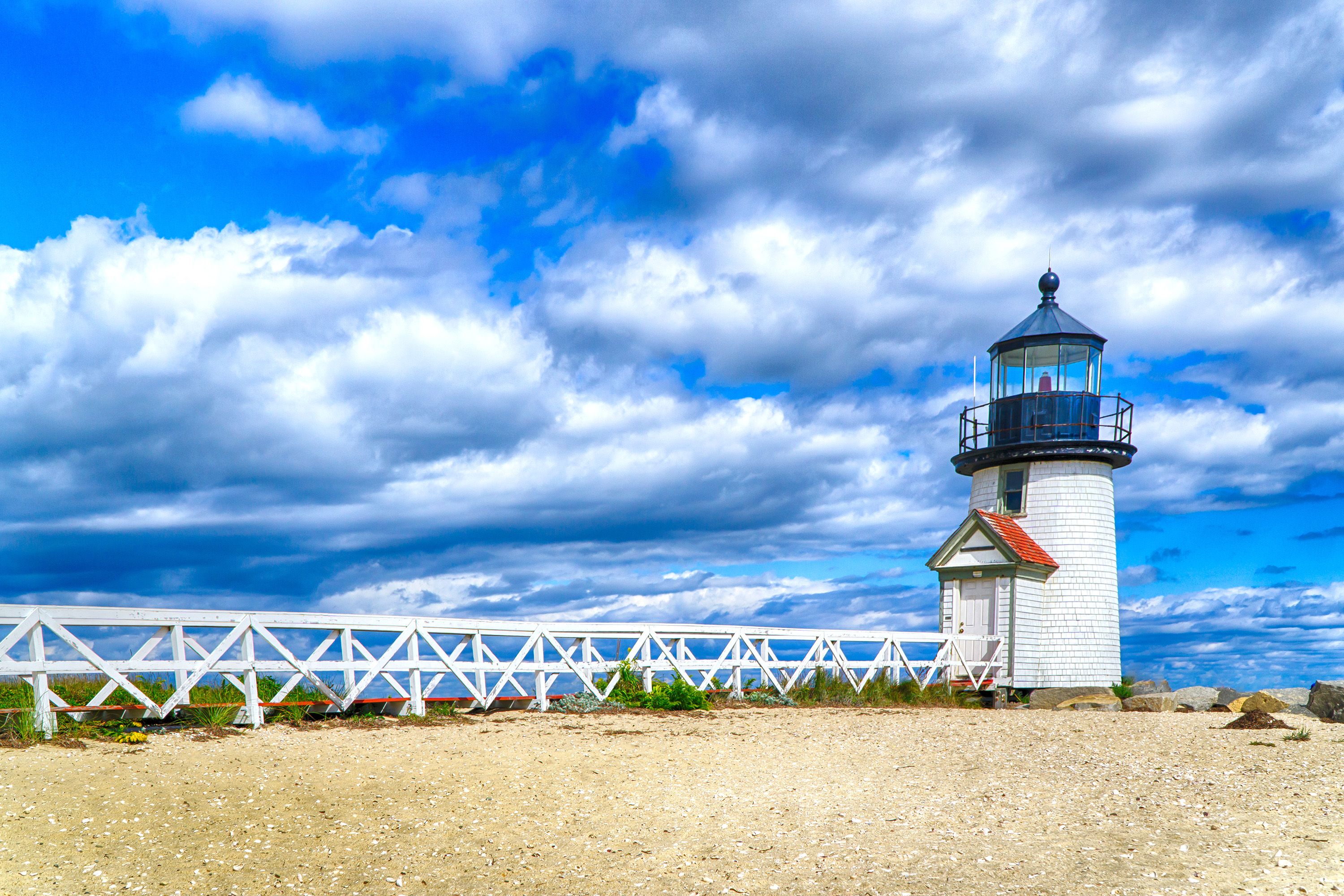 Bright blue sky and white clouds over a lighthouse and beach.