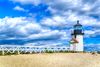 Bright blue sky and white clouds over a lighthouse and beach.