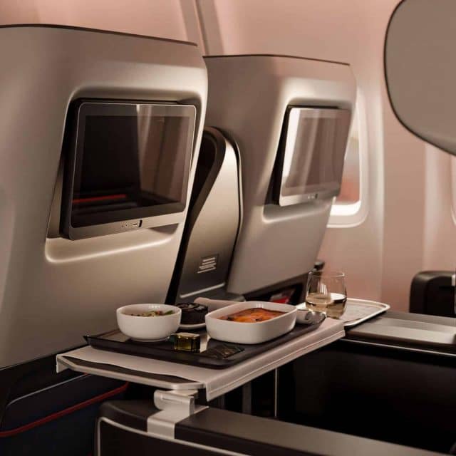 An inflight meal sits on the tray of a modern, silver-grey airline seat