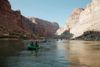 People in colorful rafts float along the Colorado River between the steep-sided canyon walls