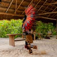 A person in a traditional colorful feathered headdress performs on the beach as part of a ceremony in Tulum, Mexico