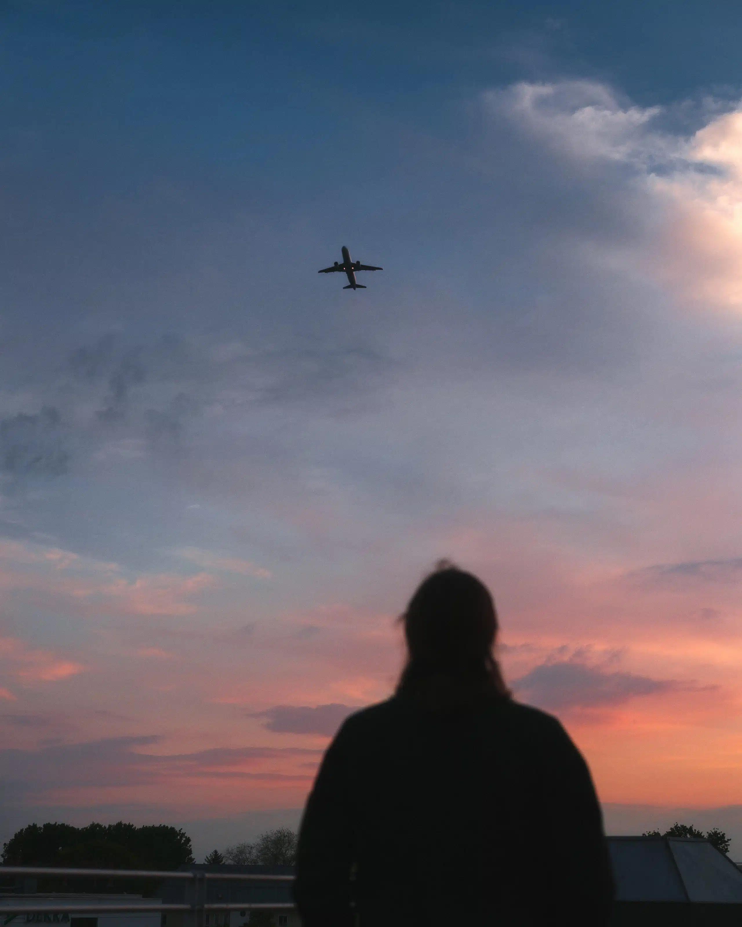 A person looks up at an airplane overhead in a pink and blue sky