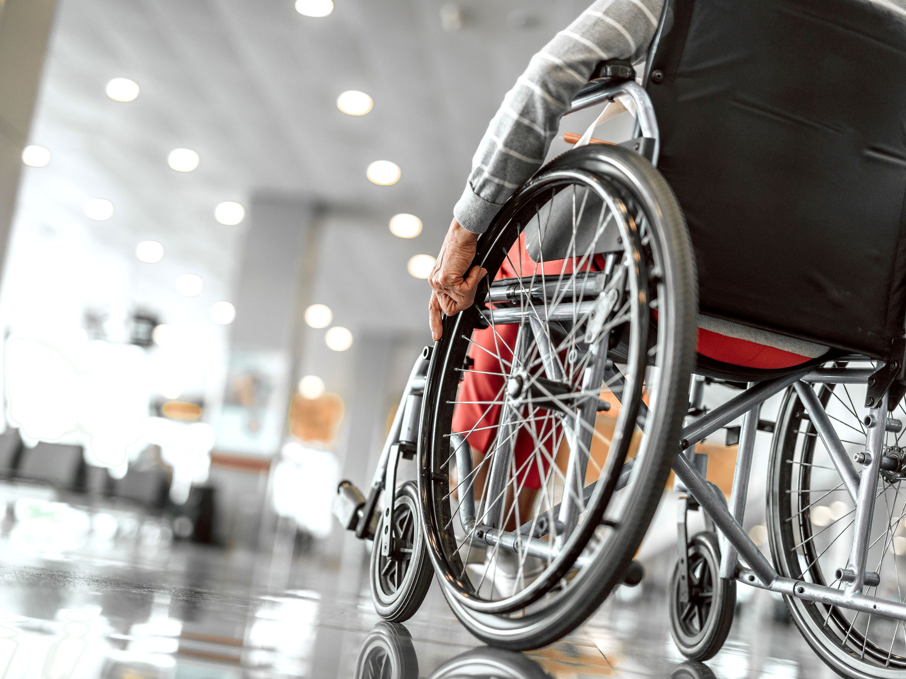 Person rests hand on wheelchair wheel in midway of airport.