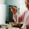 A man lifts noodles from a metal bowl with chopsticks, surrounded by smaller ceramic bowls