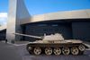 A military tank displayed outdoors in front of a modern museum building.