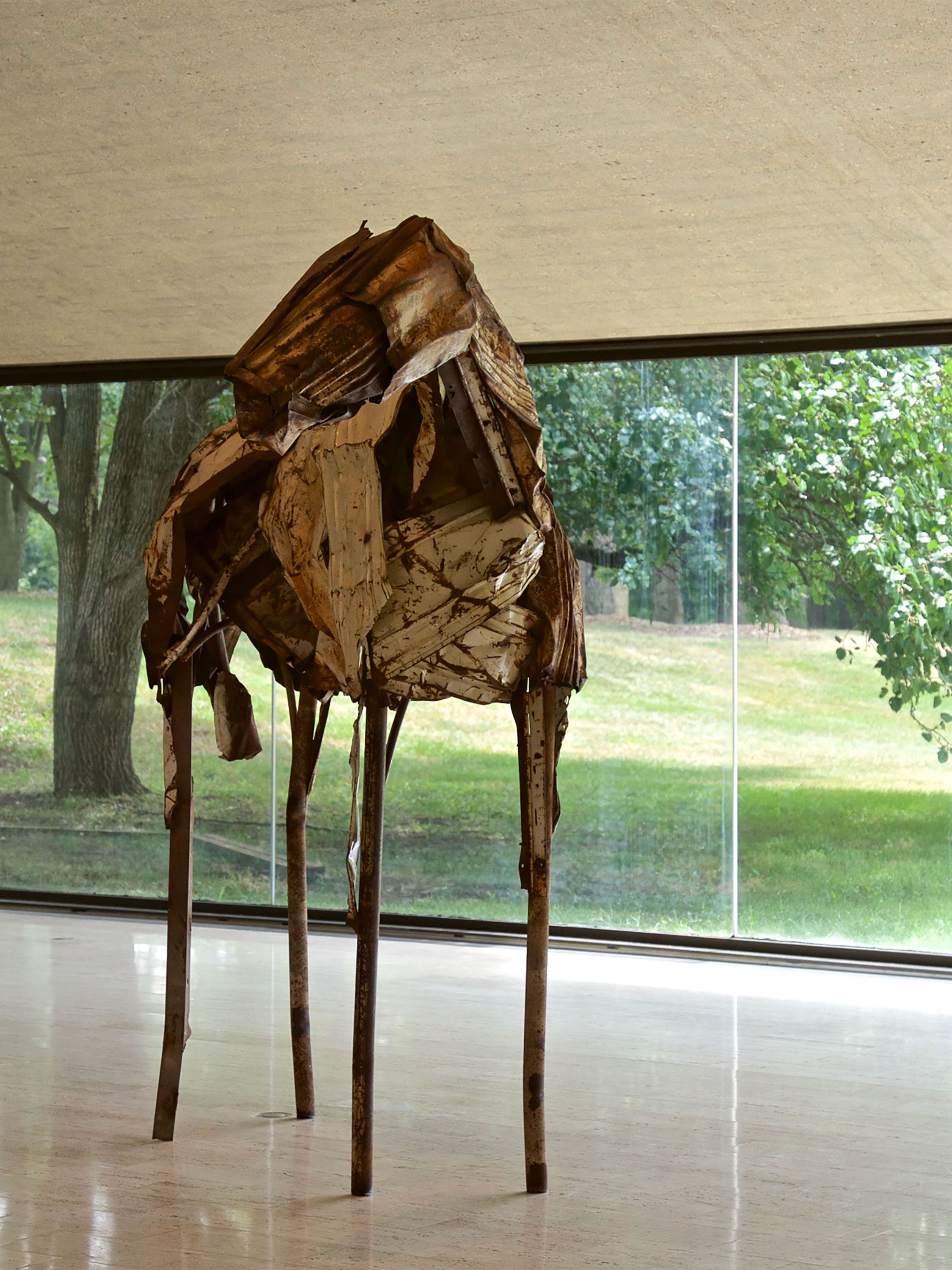 Rusted metal sculpture resembling a horse displayed in a modern gallery.