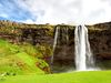 Green grass and large cliff with waterfall.