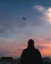 A person looks up at an airplane overhead in a pink and blue sky