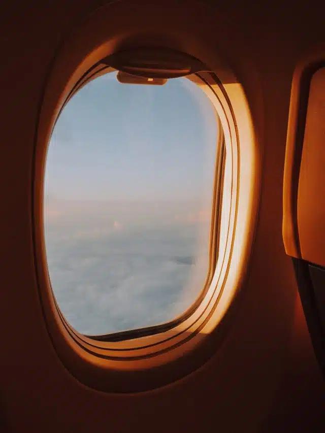 Clouds are seen through the sunlit window of an airplane at golden hour