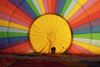 A person stands inside the envelope of a rainbow-colored hot-air balloon as it inflates