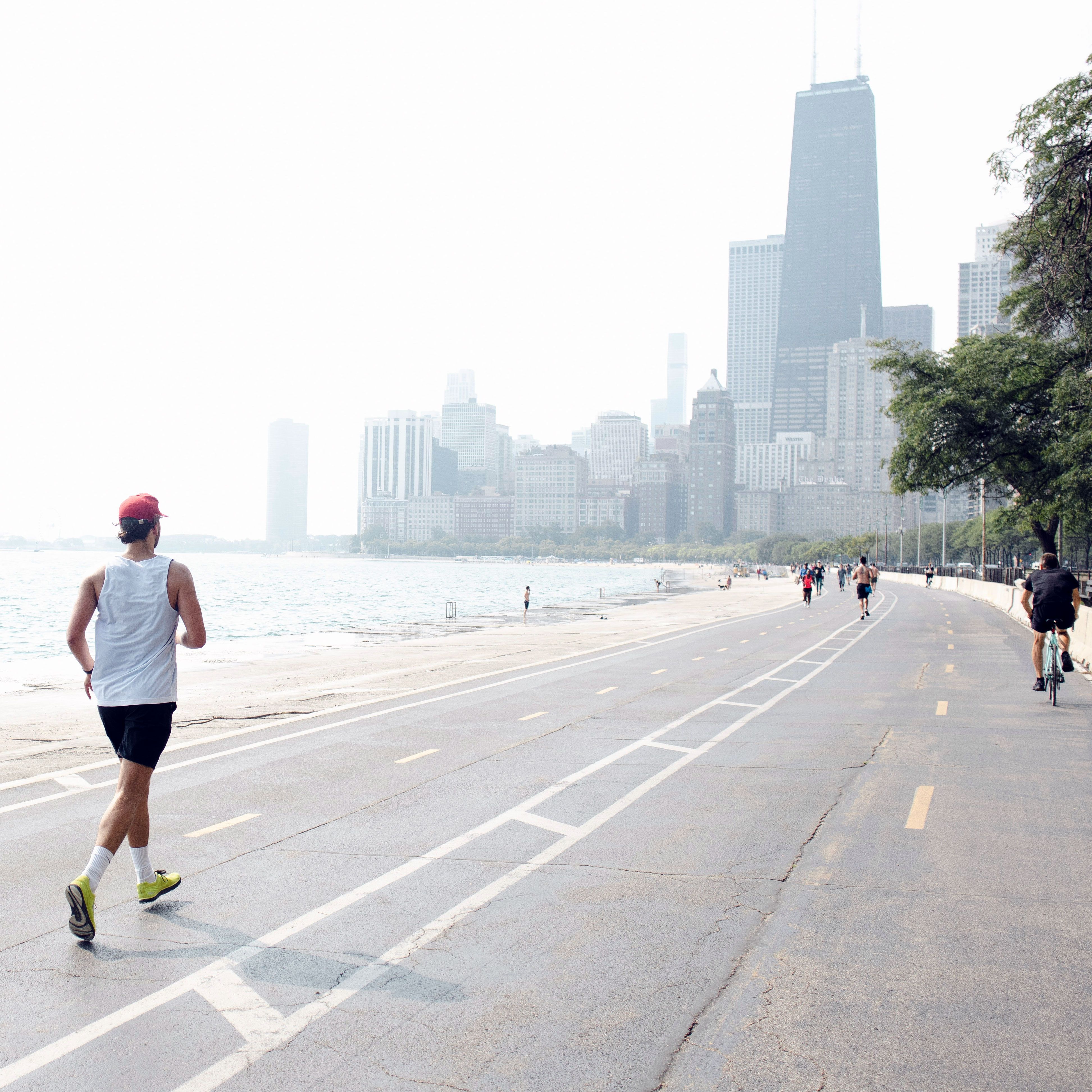 A man runs on the lakefront trail towards a downtown city.