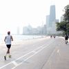 A man runs on the lakefront trail towards a downtown city.