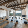 A wooden floored fitness studio with lines of yoga blocks and mats laid out. A large window leads to a view of