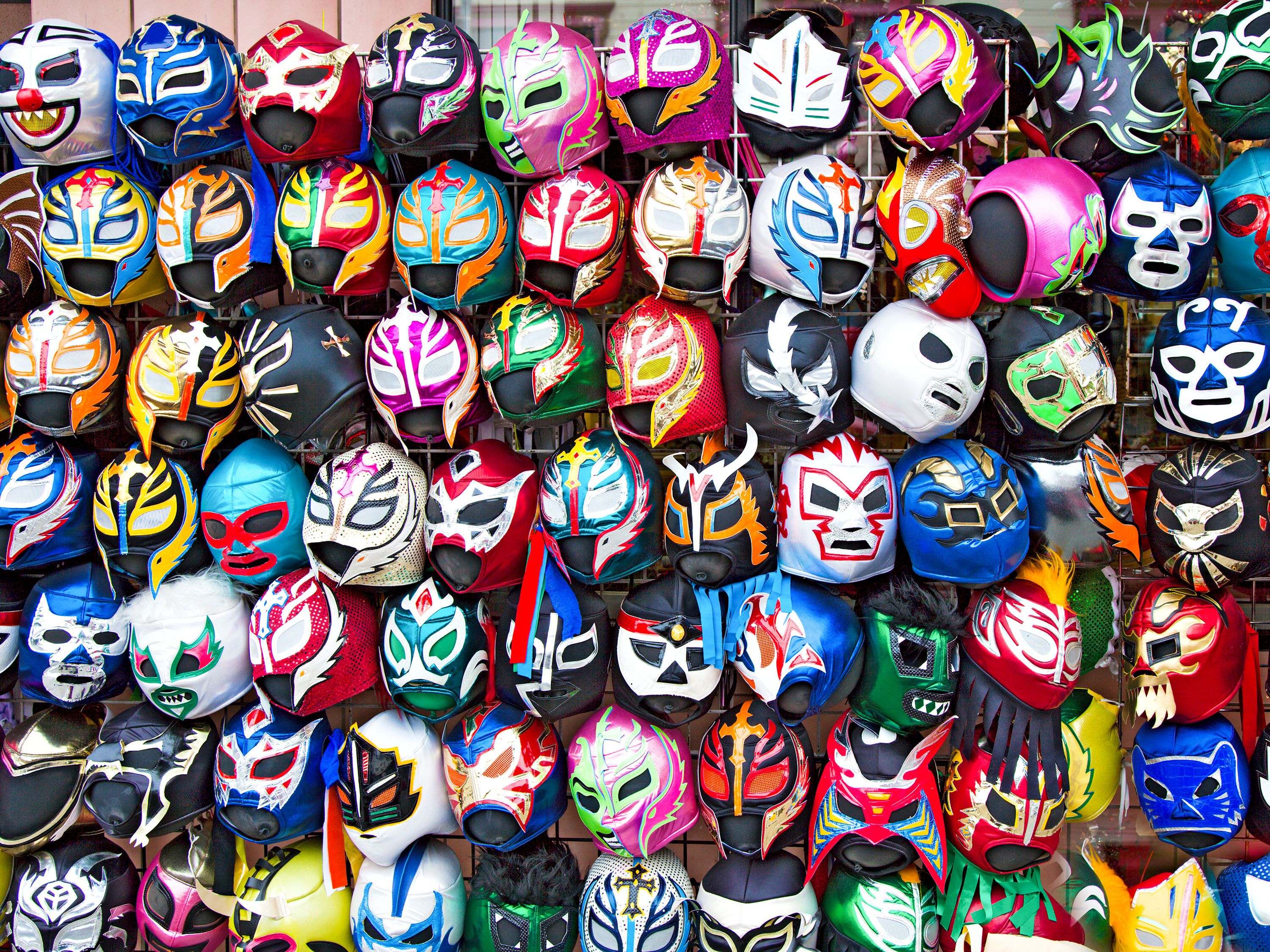 Rows of colorful masks hang on a wall.