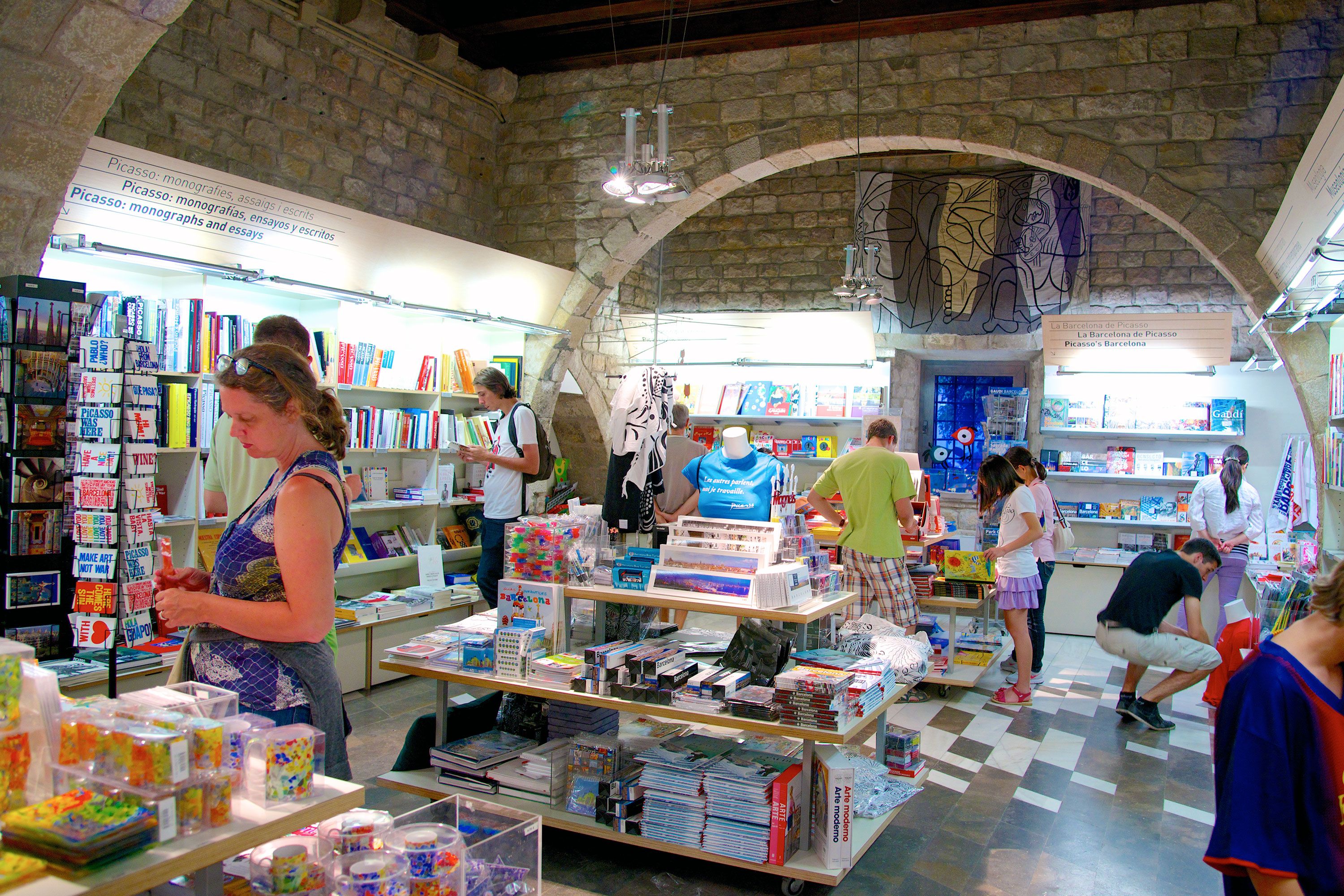 People shopping for books and art gifts inside a museum store with stone arches.