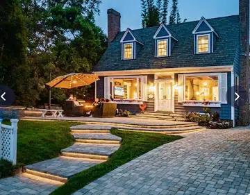 A house lit up from the inside, with a dining area outside