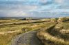 A pub stands alone in the middle of a landscape with a rocky trail in the foreground in Reeth, England.