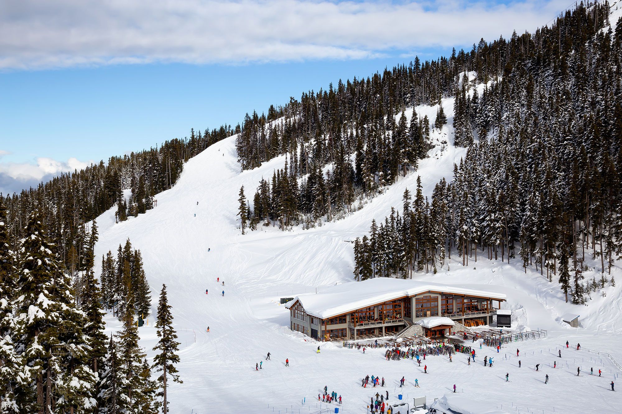 Aerial view of a big lodge on top of a snowy mountain with people walking around on a winter day in Whistler, British Columbia.