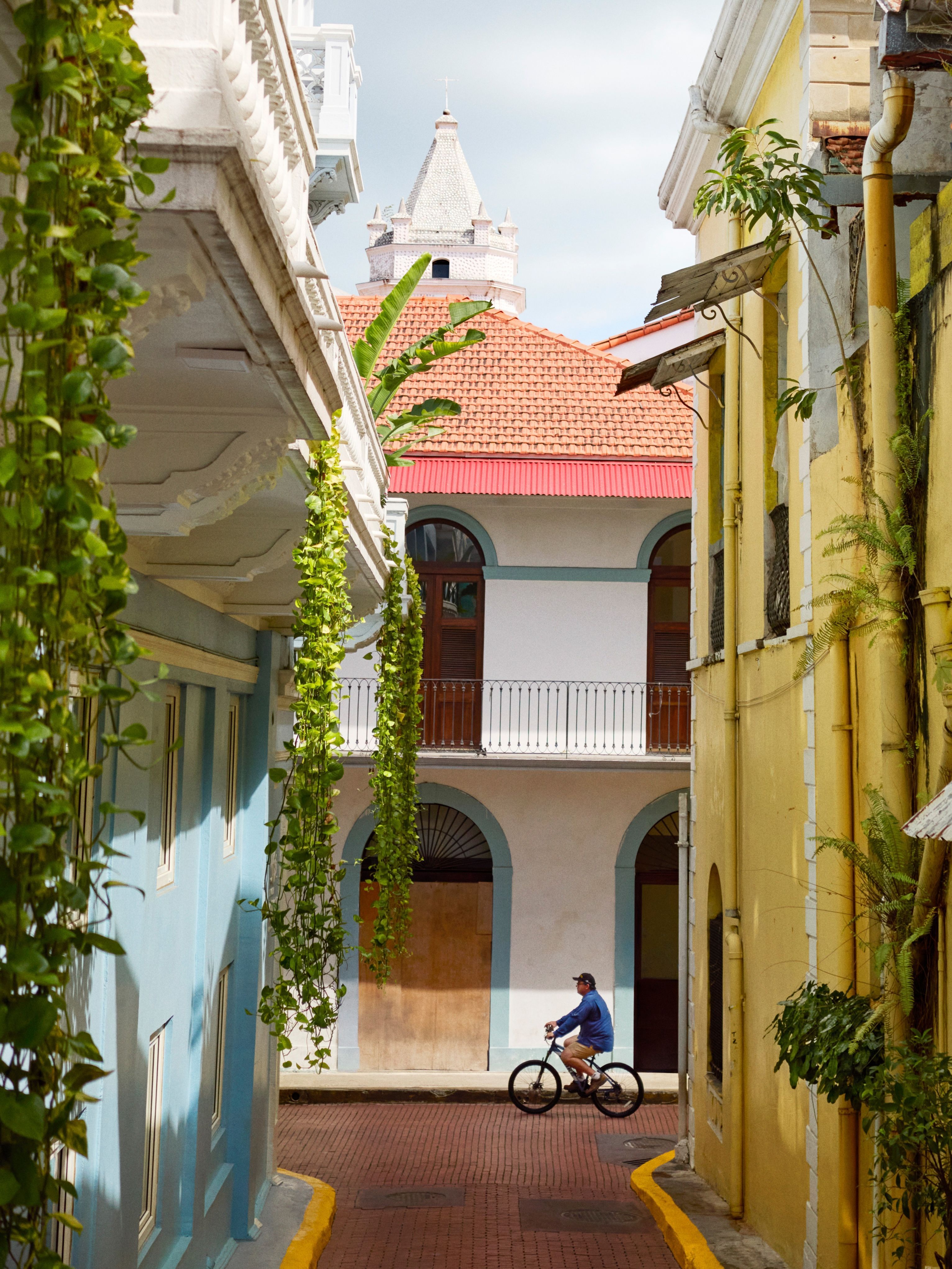 View down a narrow street in Casco Antiguo, Panama City, with pastel color buildings and a cyclist passing