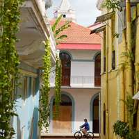 View down a narrow street in Casco Antiguo, Panama City, with pastel color buildings and a cyclist passing