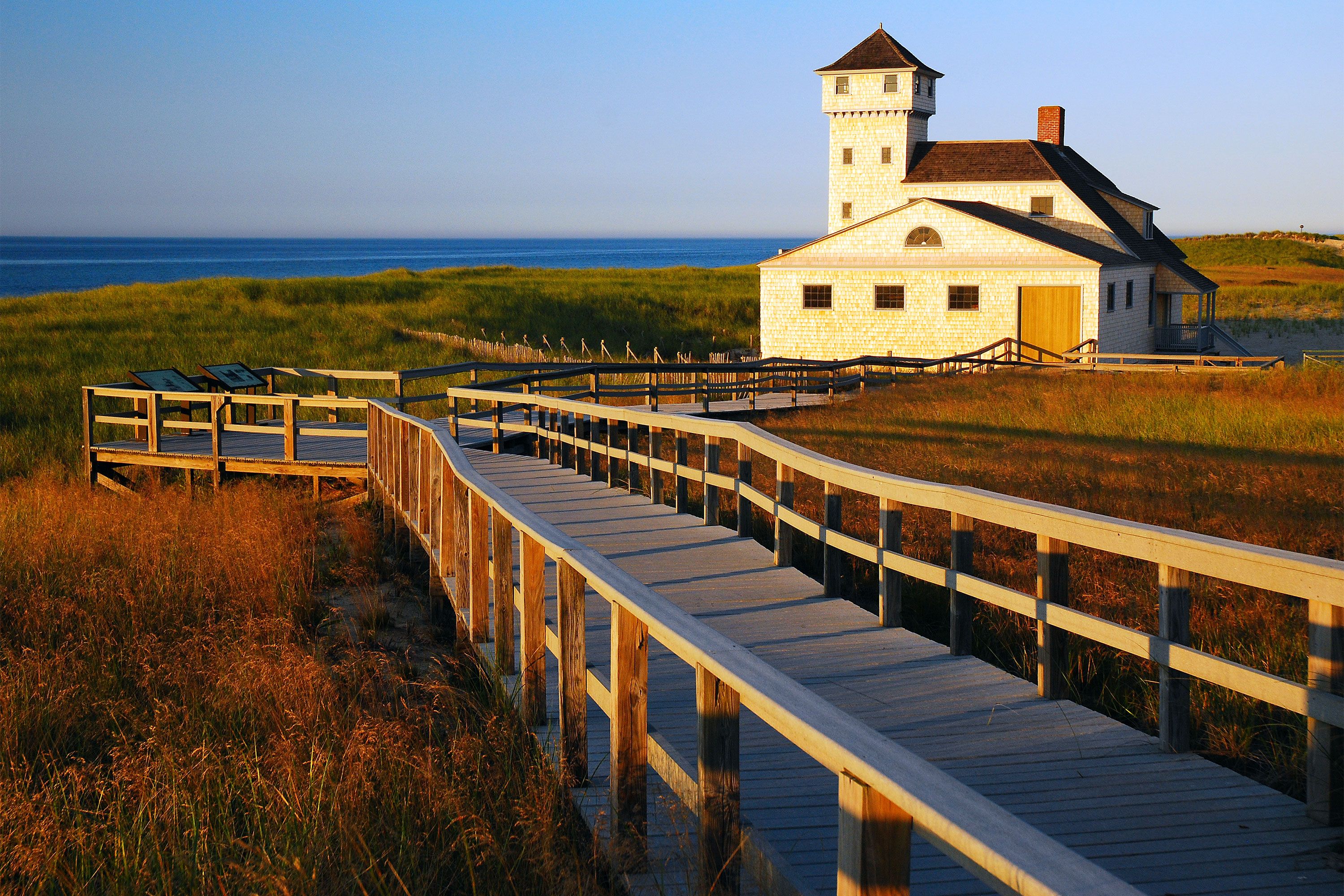 The historic wooden Race Point Coast Guard life-saving station building on sandy dunes at Cape Cod, Massachusetts, under a clear sky.