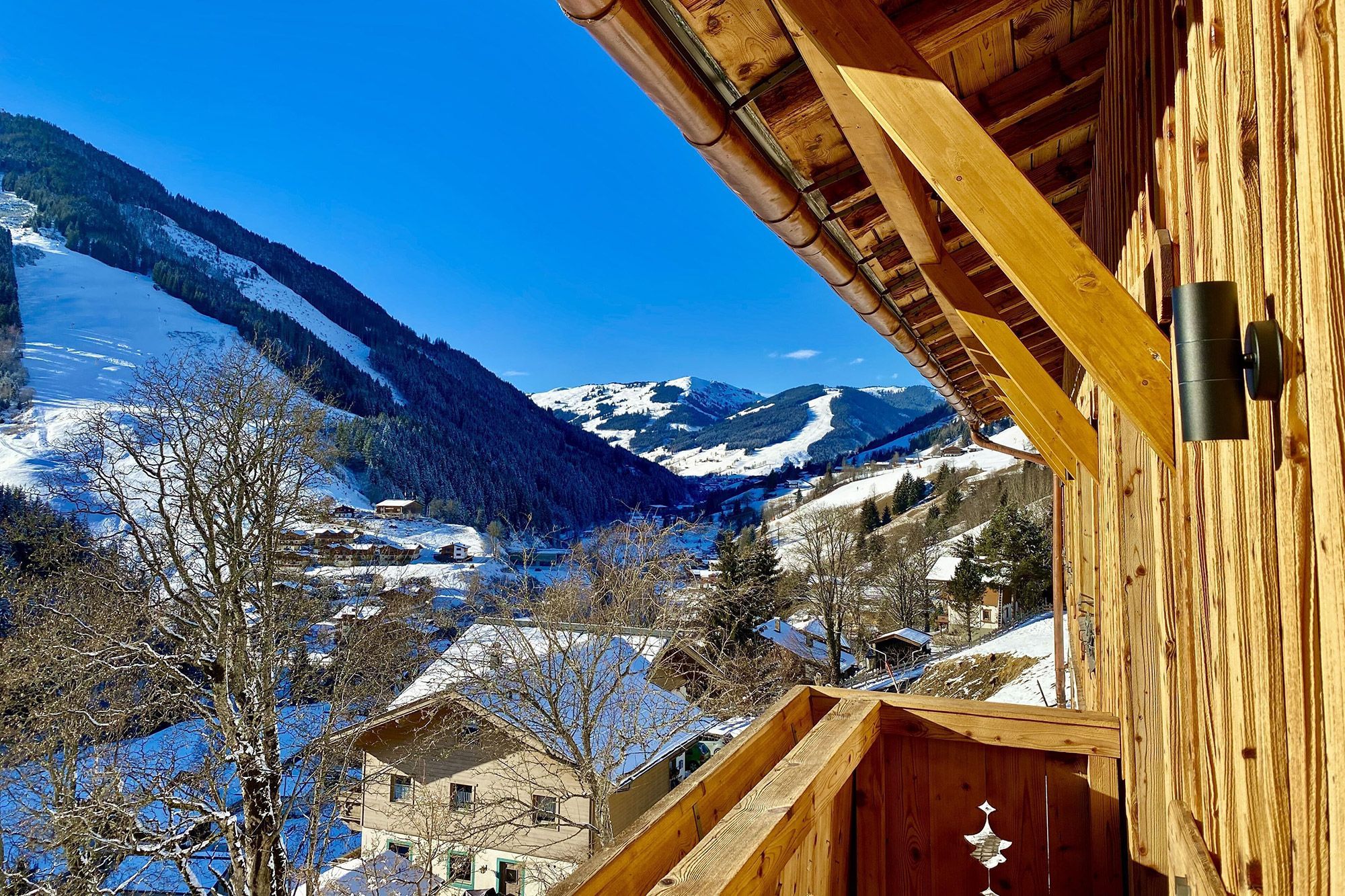 Blick vom Balkon eines Holzhauses auf das verschneite Bergpanorama  