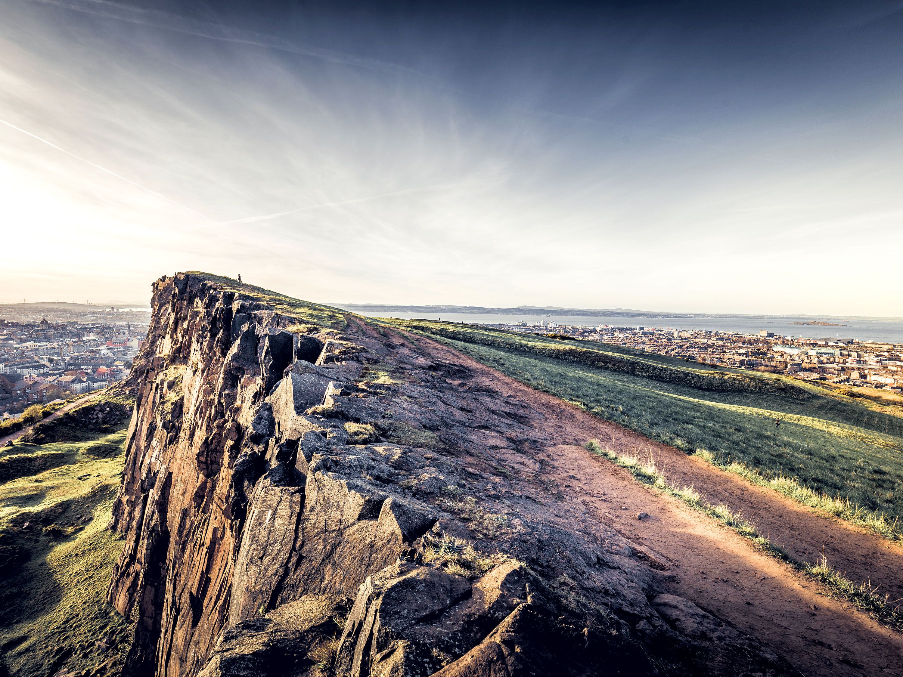 Cliff over mossy green and city down below.