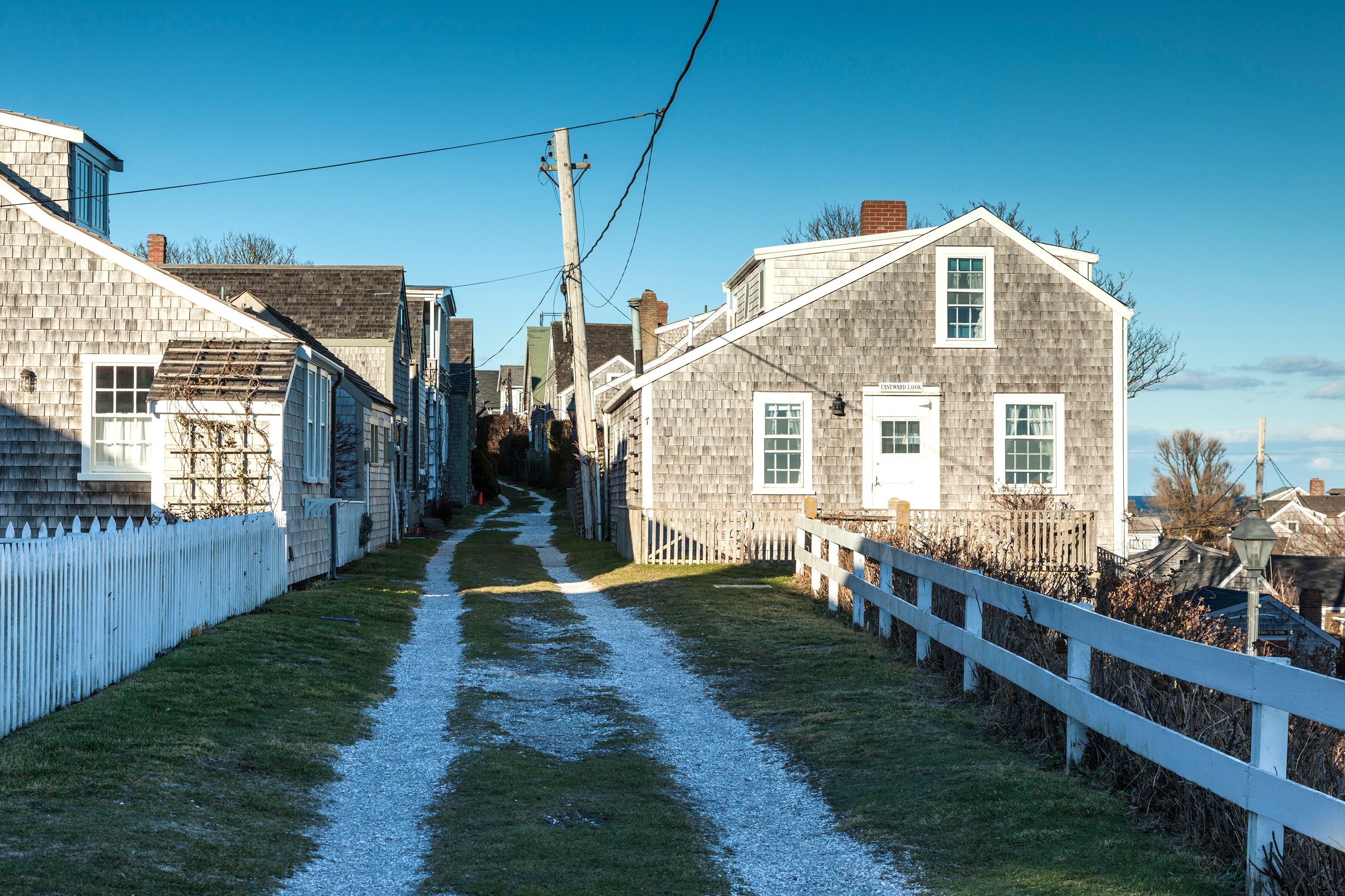 Gravel drive between beach cottages and a white picket fence.