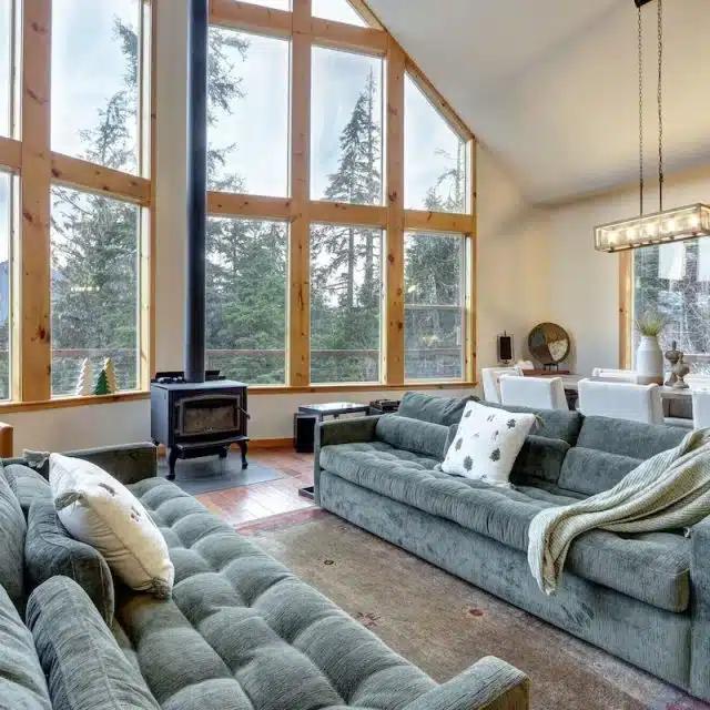 The interior of a Vrbo with huge windows looking onto a forest, with two giant sofas facing each other