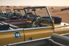 Old Land Rover vehicles sit in a row across sandy desert dunes in the United Arab Emirates.