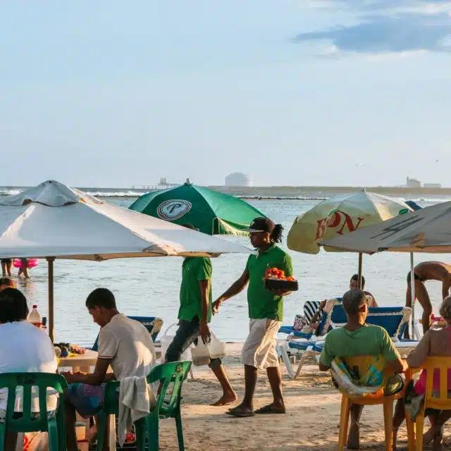 Snacks are served to guests relaxing under green and white umbrellas on the beach