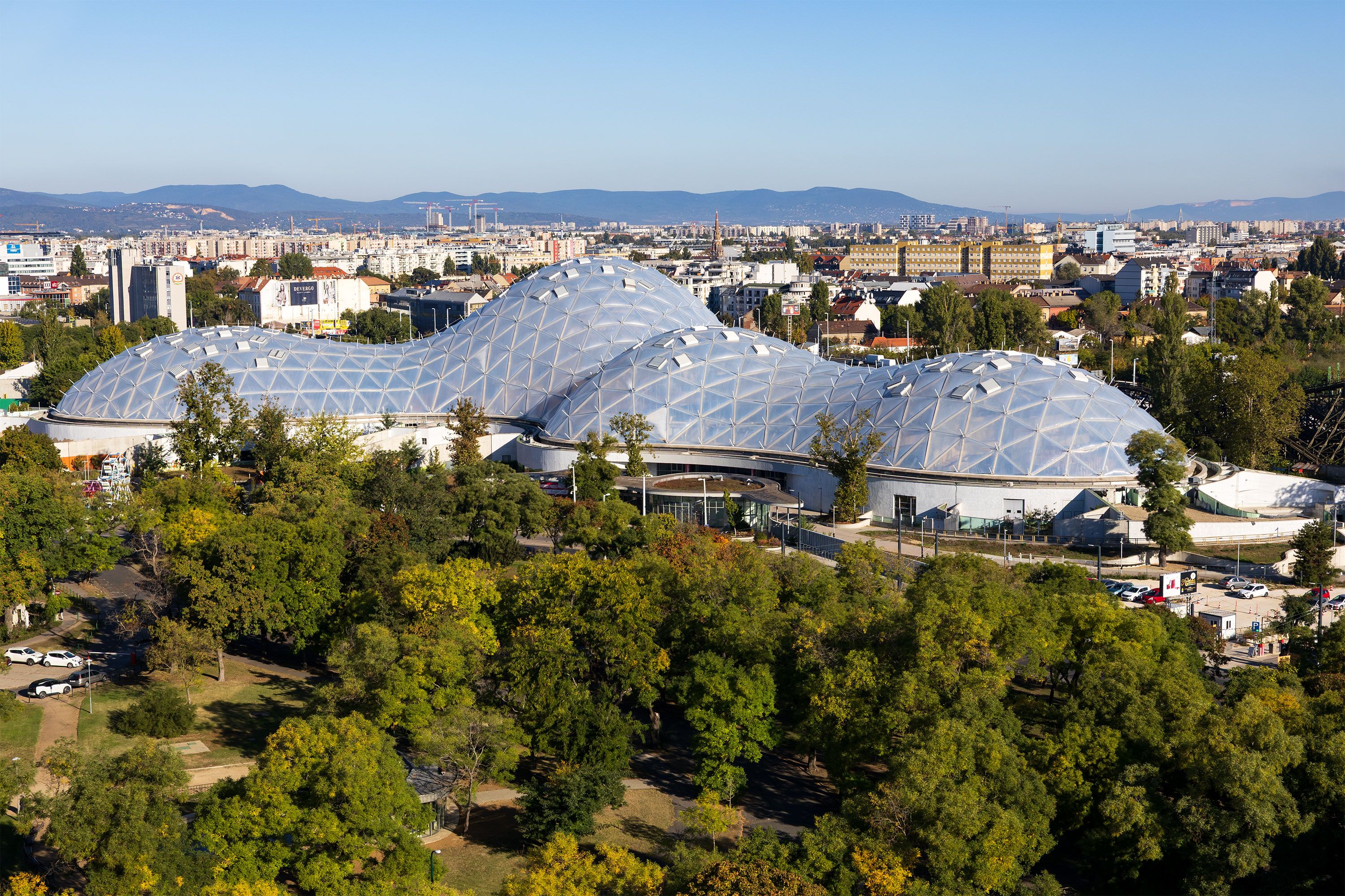A  large curved glass-and-metal dome surrounded by trees and parkland.