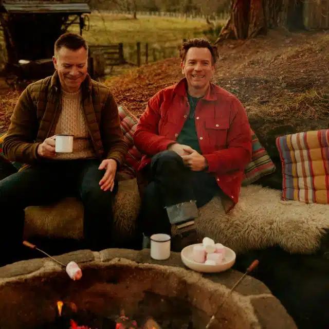 Brothers Colin McGregor and Ewan McGregor sit on sheepskin rungs by a firepit, with marshmallows grilling and hot chocolates at the ready, at the Dell of Abernethy, Scotland