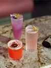 Colorful drinks with fruit and floral garnishes are served up in various types of glasses on a marble table