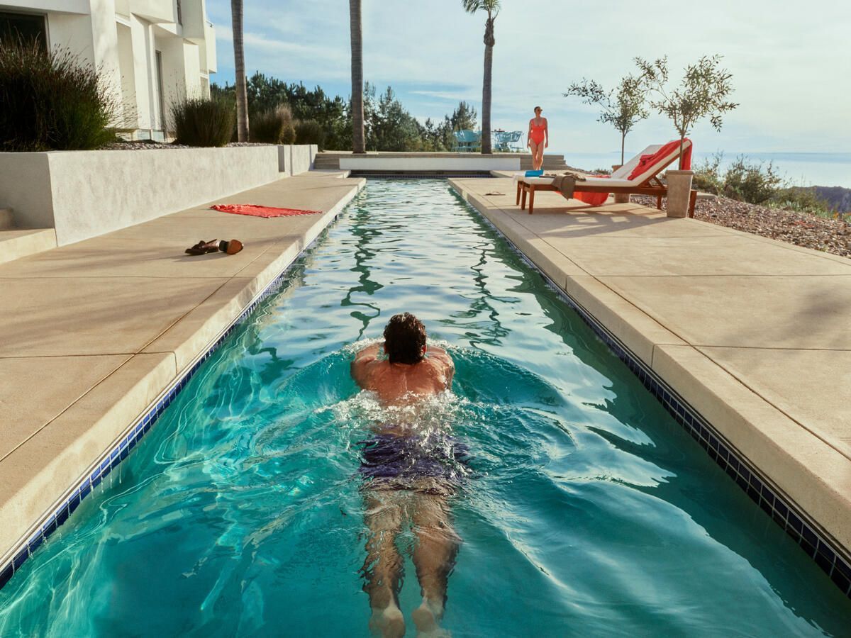 A person swimming down a long lap pool at a Vrbo, with the sea visible to one side