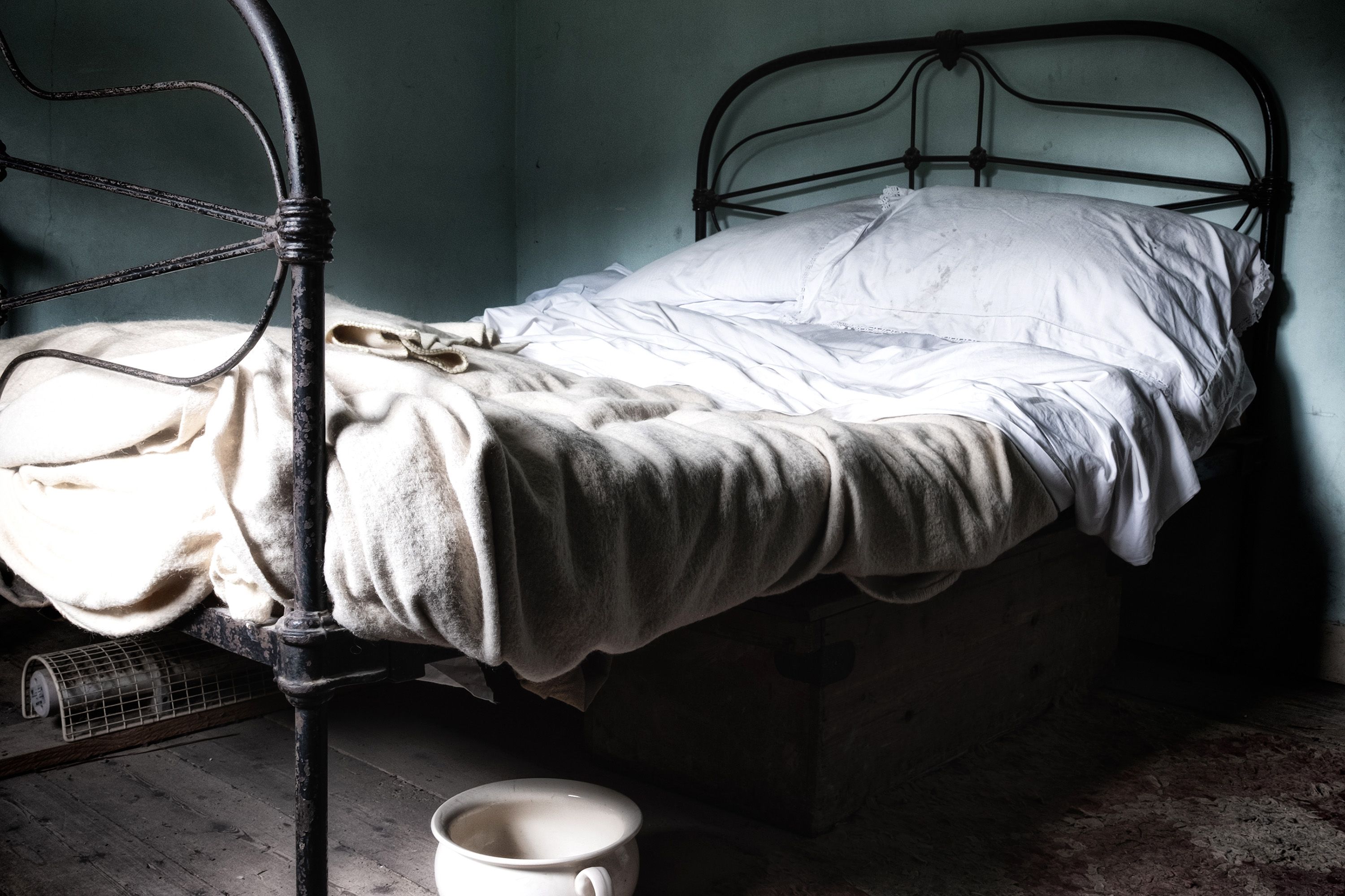 An antique bed with white bedding and chamber pot underneath.