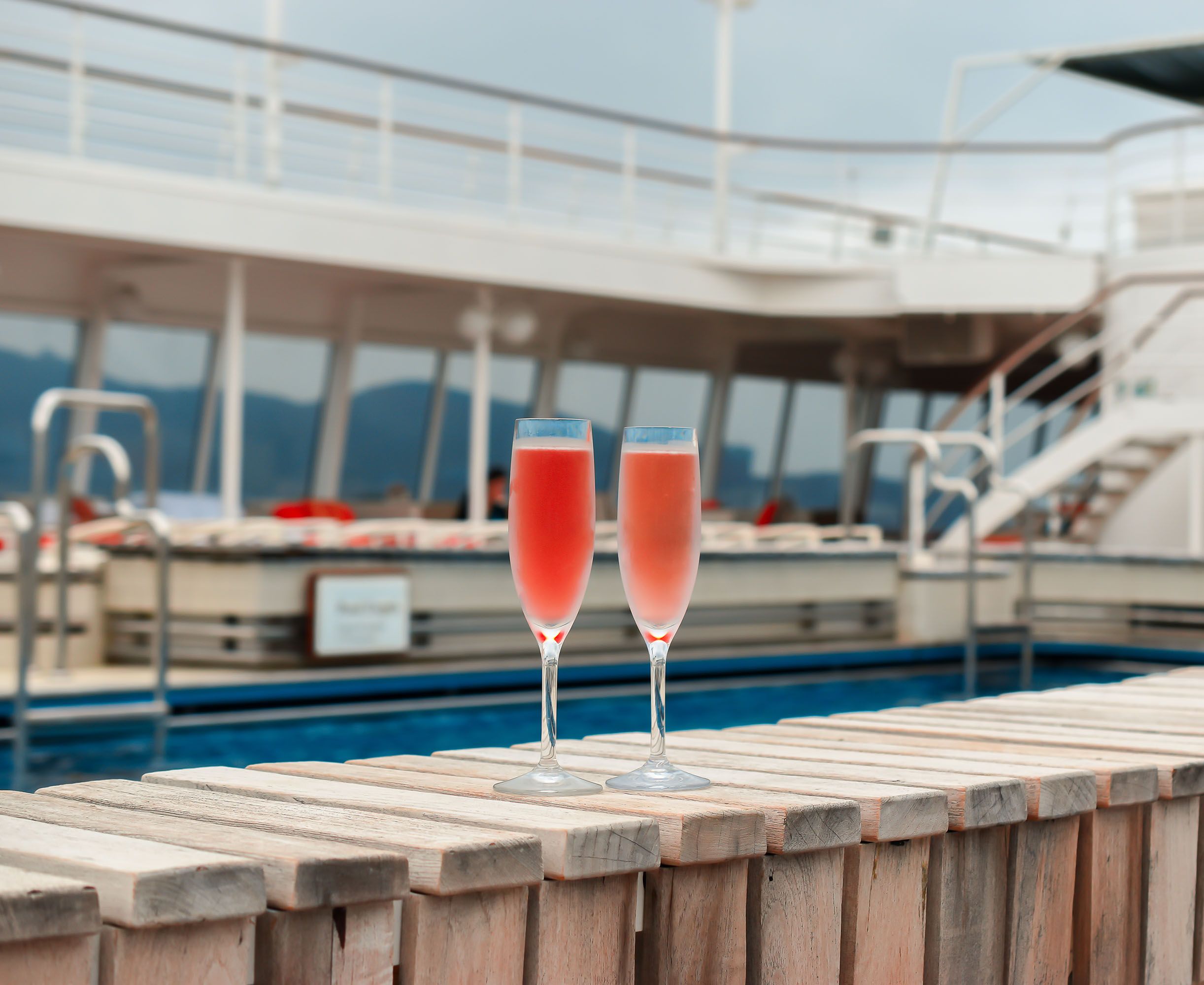 Two champagne flute glasses filled with a pink-colored drink placed on a wooden railing.