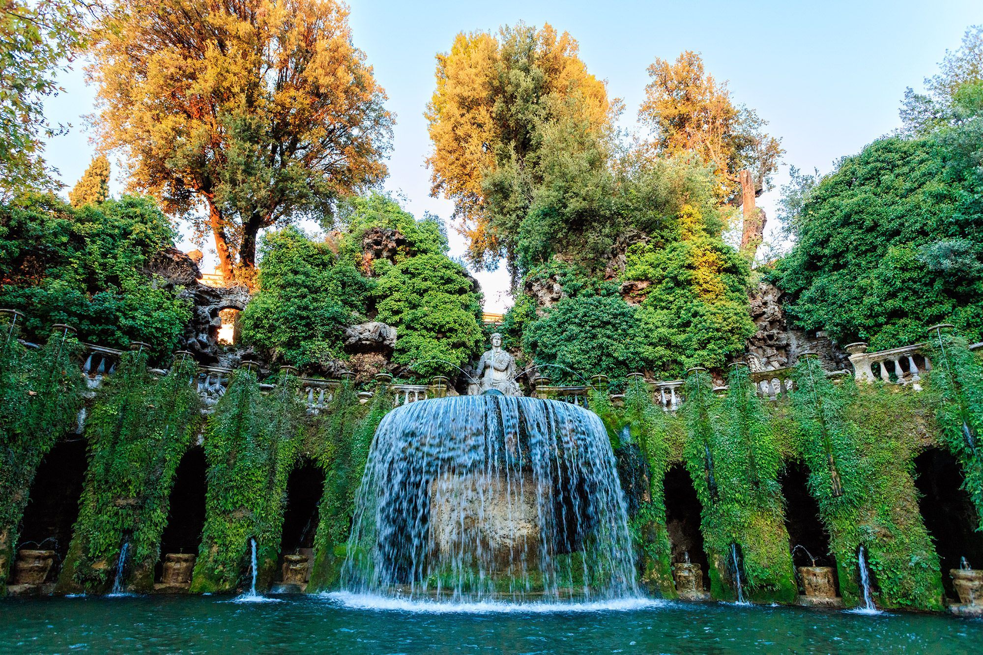 The Oval Fountain at Villa d'Este in Tivoli surrounded by green vines and trees.